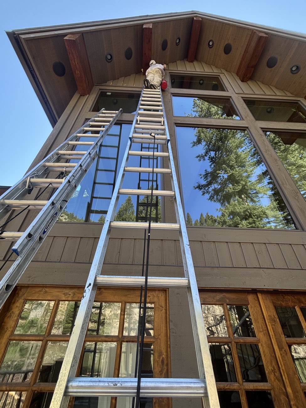Painter on a tall extension ladder at the gable of a mountain home