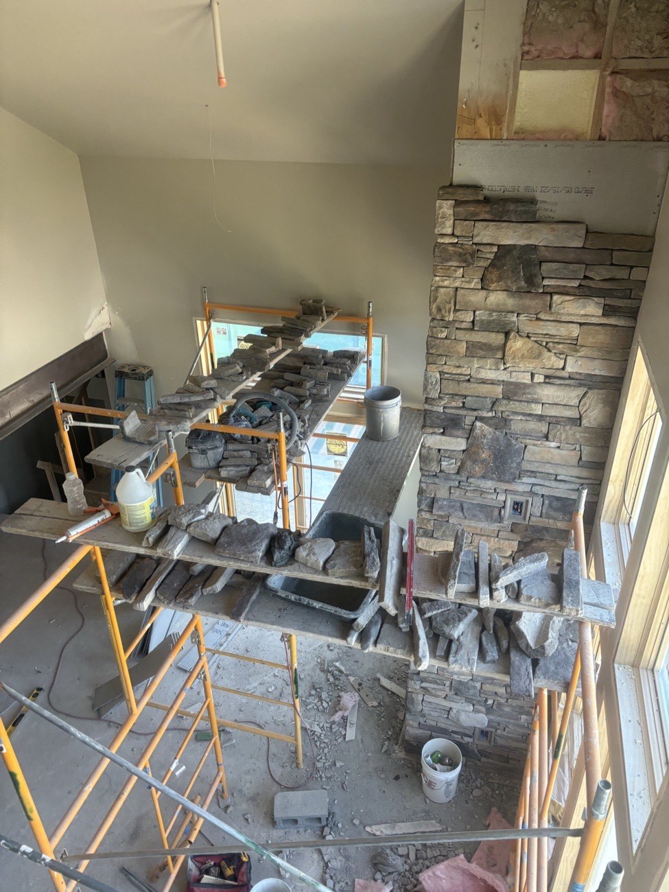 Stacked stone veneer going up on a tall fireplace wall, with scaffolding