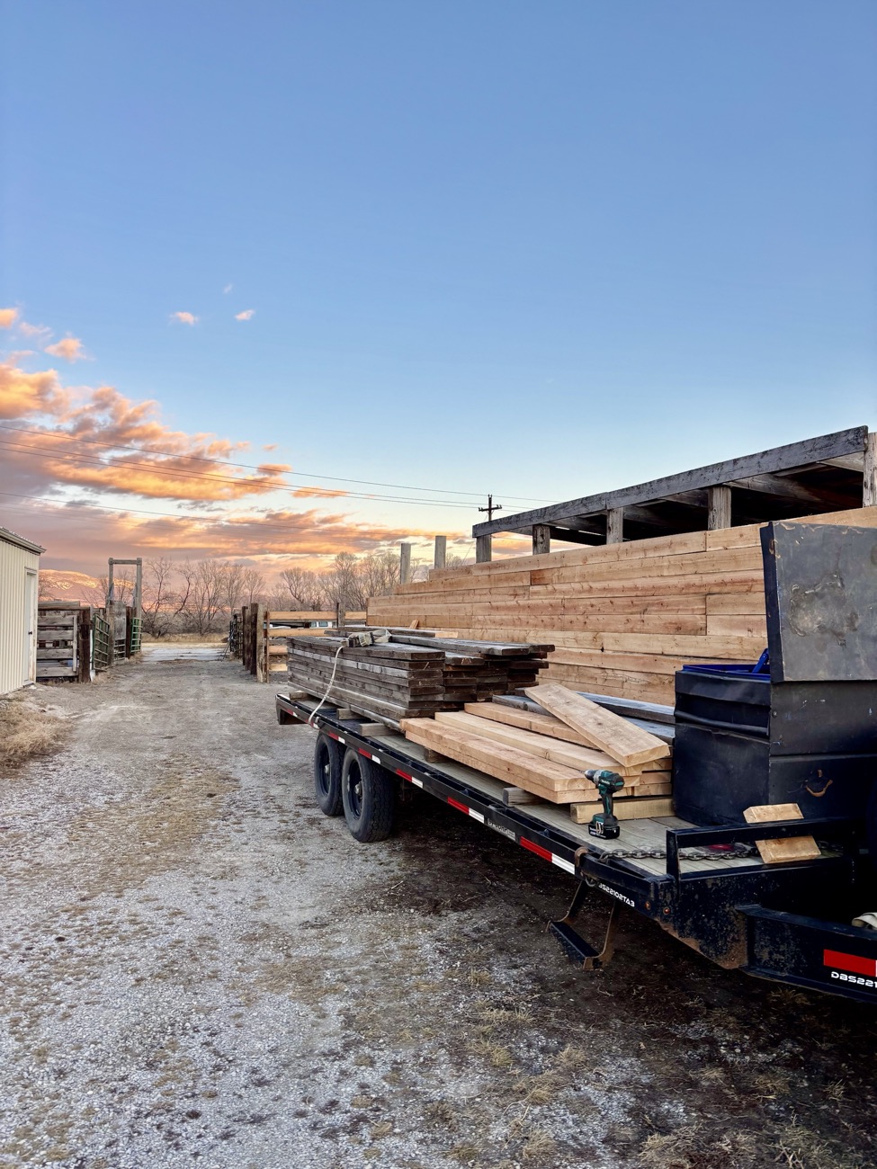 Trailer loaded with lumber beside new board fencing at sunset