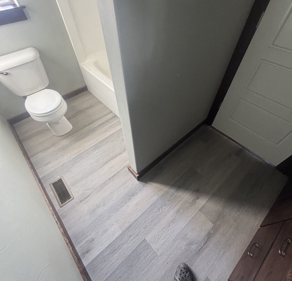 Finished gray vinyl plank flooring in the bathroom, with the toilet back in place